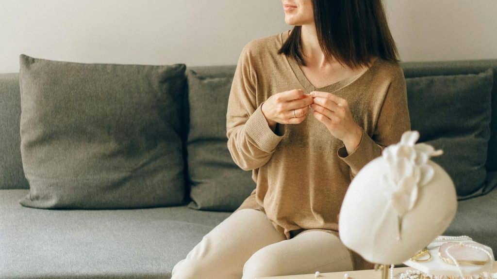 A woman sitting on a couch holding jewelry in her hands.