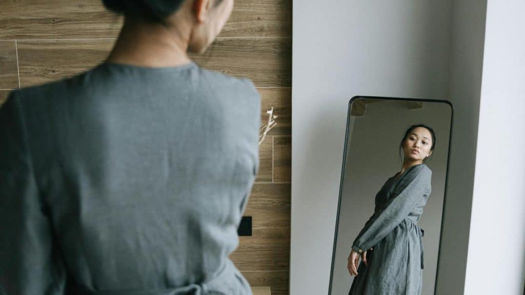 A woman looking at her reflection in a full-length mirror.