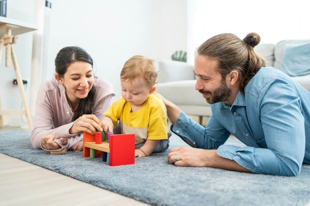 The parents are playing with their toddler in the living room.