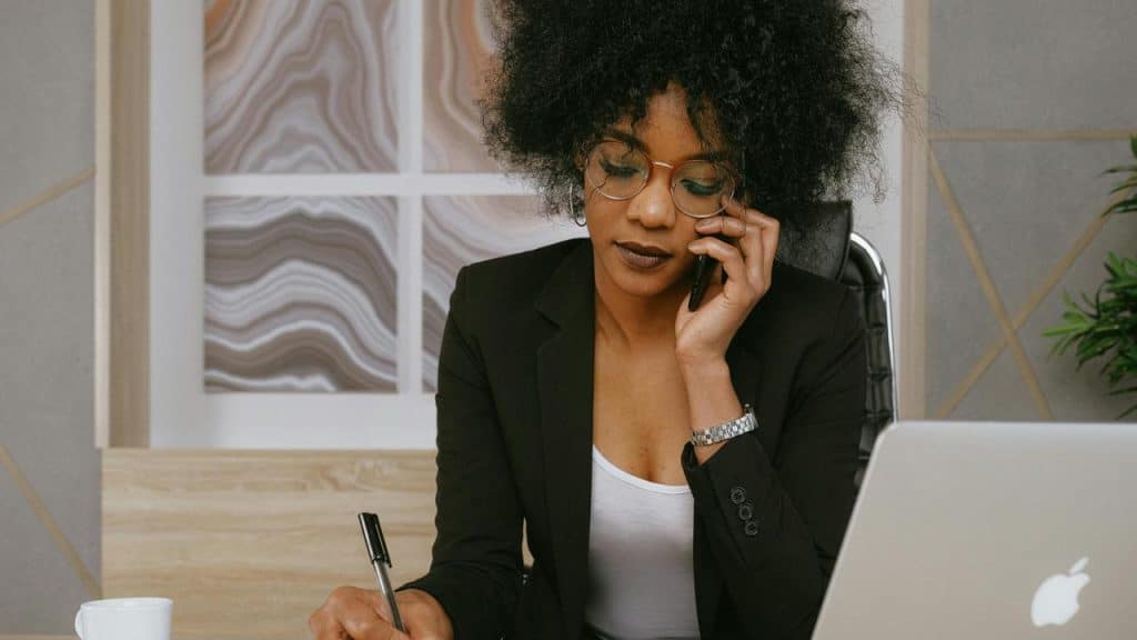 A woman sitting at a desk talking on the phone and writing notes.