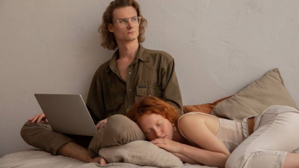 Man at his laptop working late while his partner is asleep and is tired of waiting