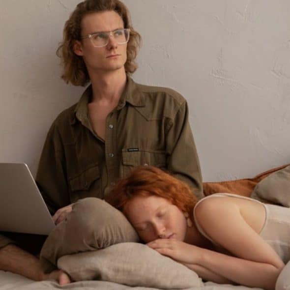 Man at his laptop working late while his partner is asleep and is tired of waiting