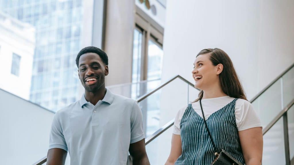 A man and woman smiling while walking down a staircase indoors.