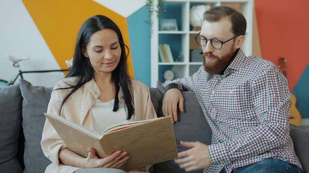  A couple sitting on a couch and looking through an album.