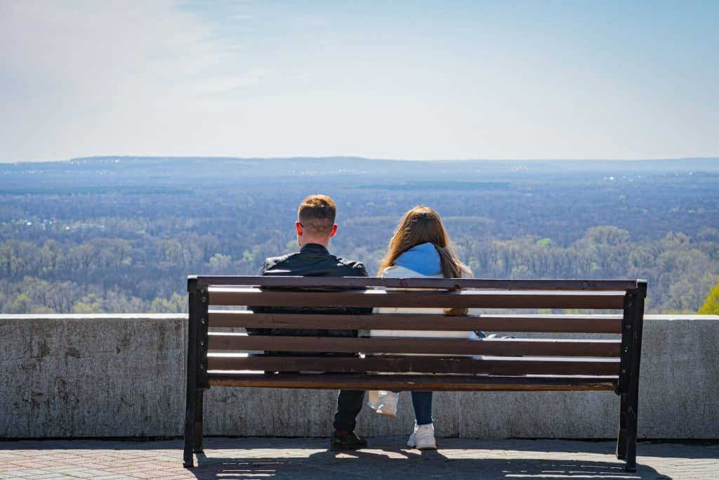 A man and woman sitting on a bench overlooking a city.