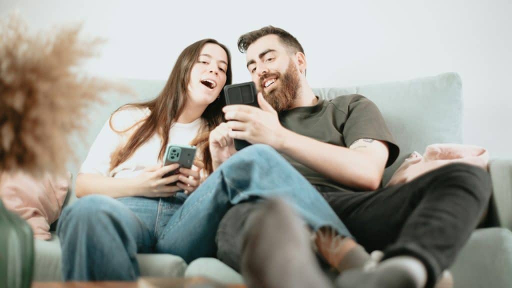 A couple using phones while sitting on a couch.