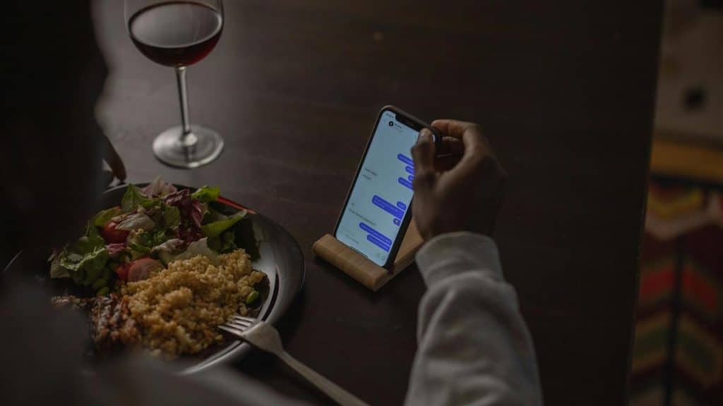 A person eating dinner while texting on a smartphone.