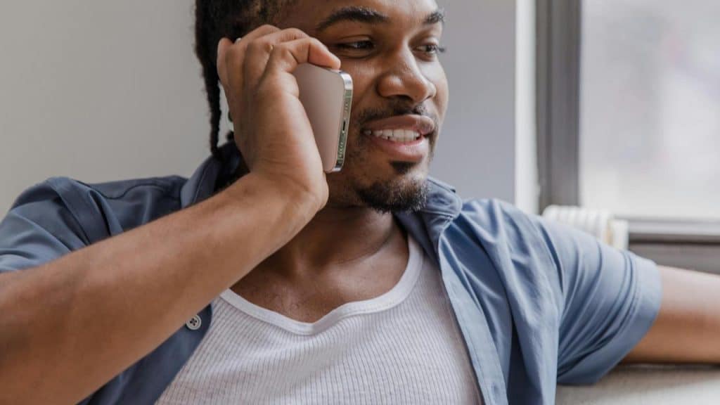 A man smiling while talking on his phone near a window.