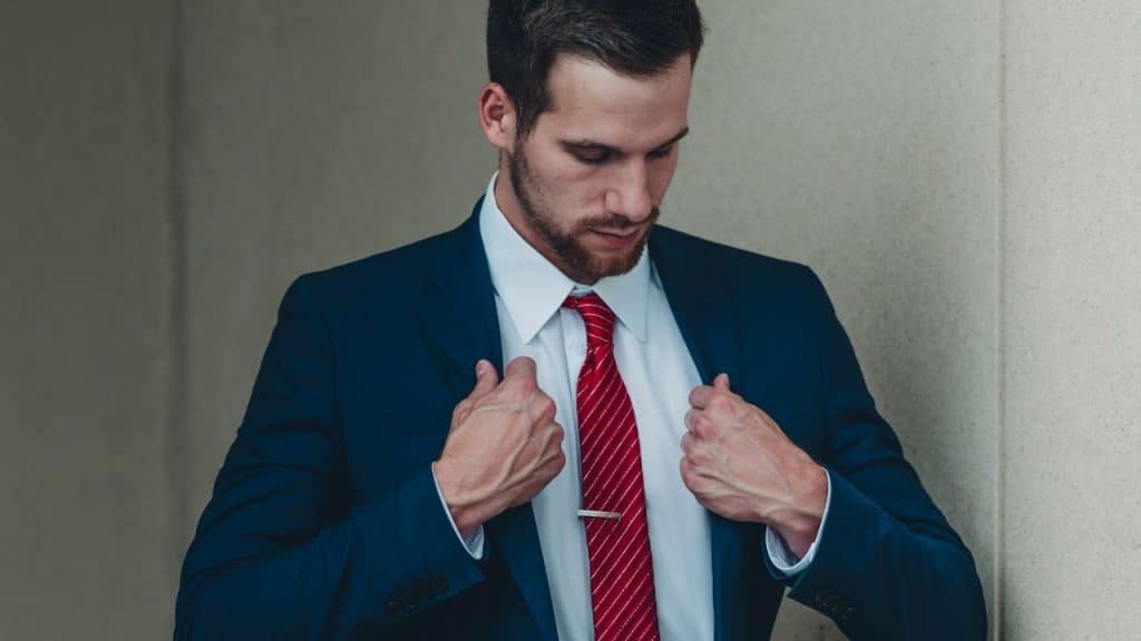 Man in a navy suit and red tie adjusting his lapels.
