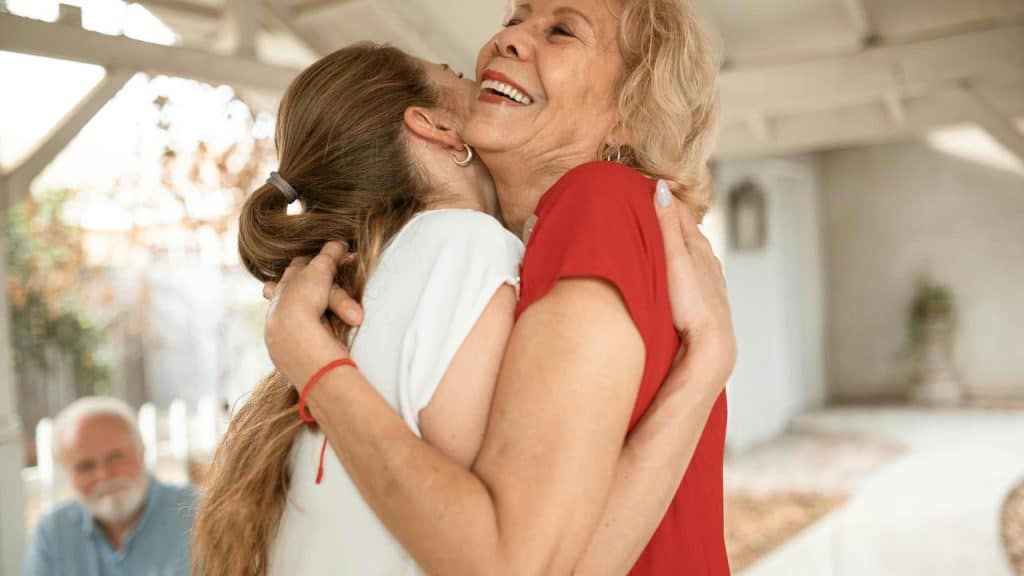 An older woman hugging a younger woman outdoors while smiling.