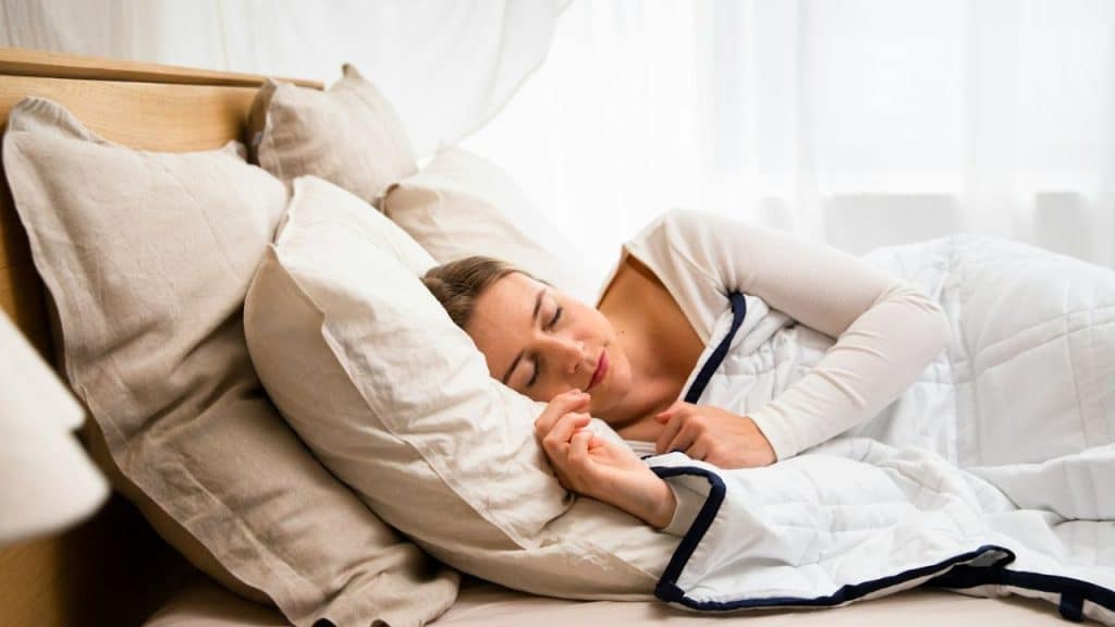 Woman is sleeping on her side in a bed, head resting on a pillow.