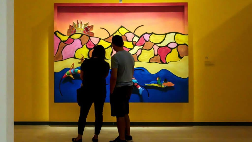 A couple viewing a colorful painting in an art gallery.