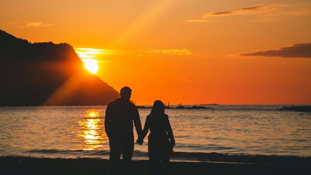 A couple holding hands on the beach at sunset.