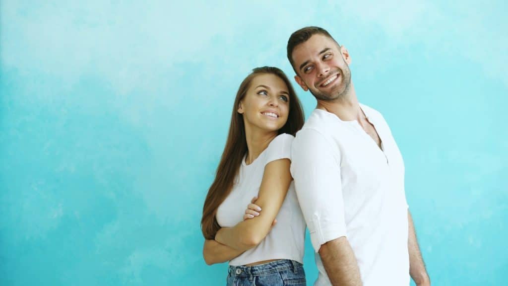 A couple standing back-to-back against a blue wall.