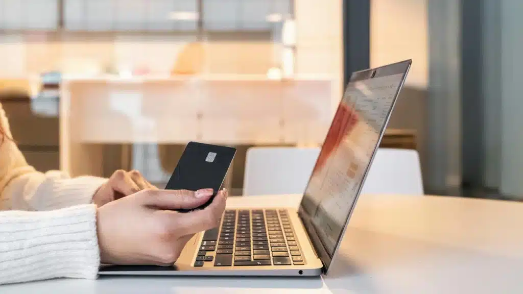 A person holding a credit card while using a laptop at a desk.