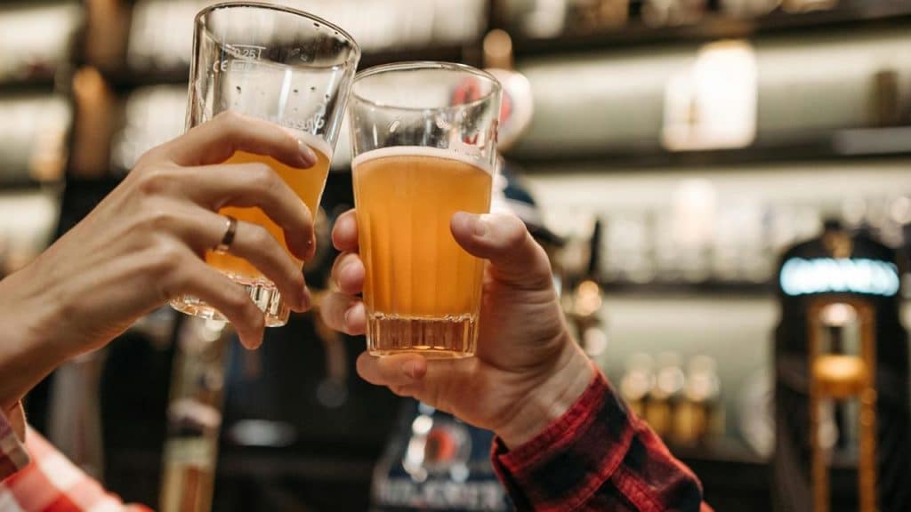 A close-up of two people clinking glasses of beer at a bar.