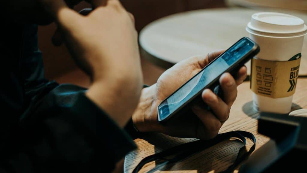 A person holding a smartphone next to a coffee cup on a café table.
