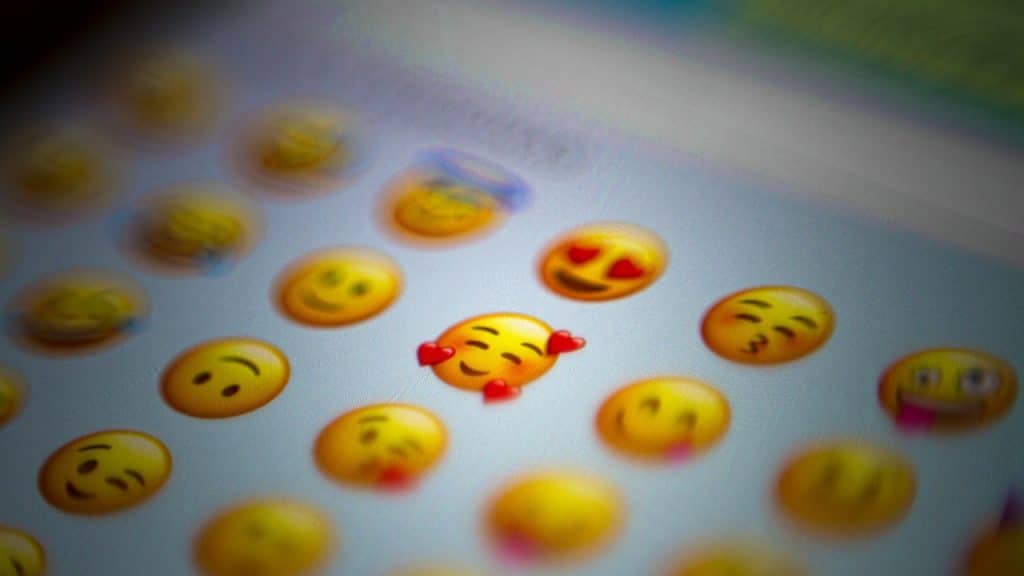 A screen showing a variety of emojis, with a heart-eyes emoji and a three-hearts emoji standing out sharply against a blurred background.