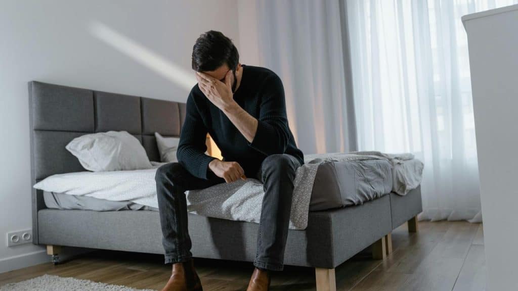 A man sitting on a bed with his head in his hand.