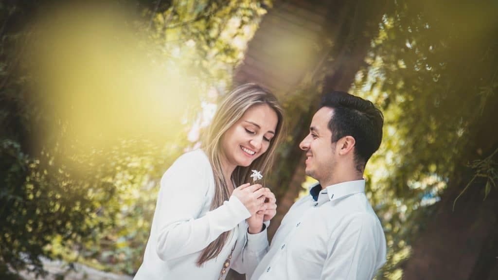 A man giving a white flower to a woman surrounded by green trees.