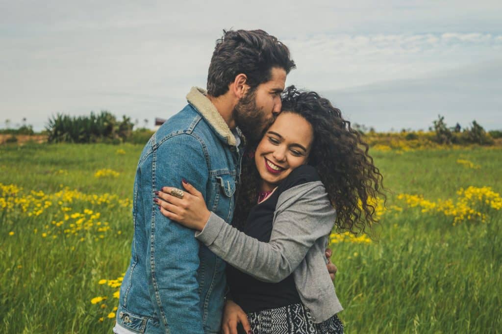 The man is kissing the woman in a field of flowers.