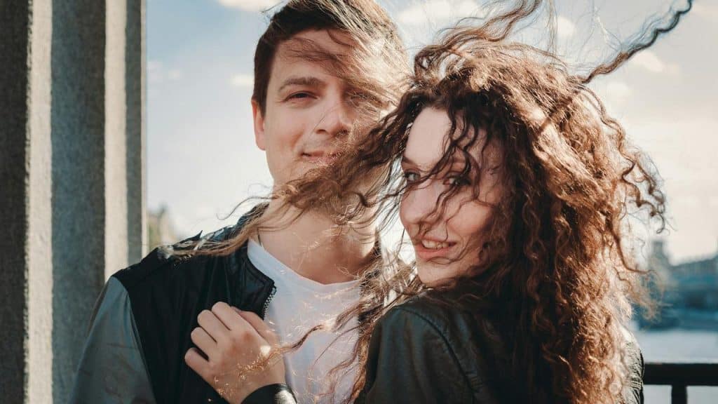 A smiling couple standing close together on a windy day.