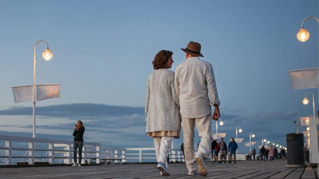 Couple holding hands and walking away on a boardwalk at dusk with streetlights.