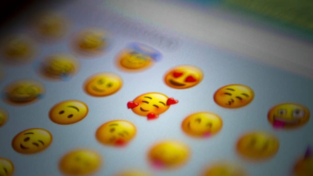 Close-up of a screen showing various emojis, with a smiling face with hearts emoji in focus and surrounded by motion blur.