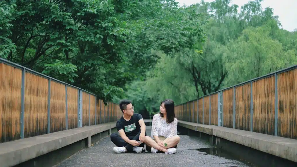 A man and woman sitting on the floor near trees.