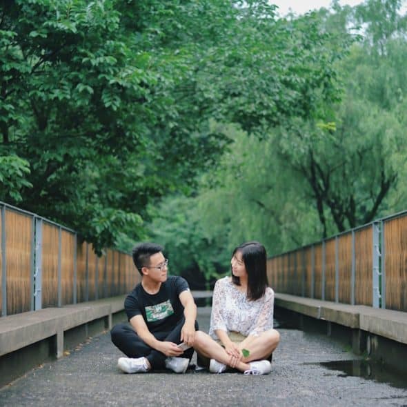 A man and woman sitting on the floor near trees.