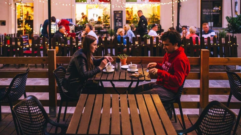 A couple sitting at an outdoor café in the evening with string lights.