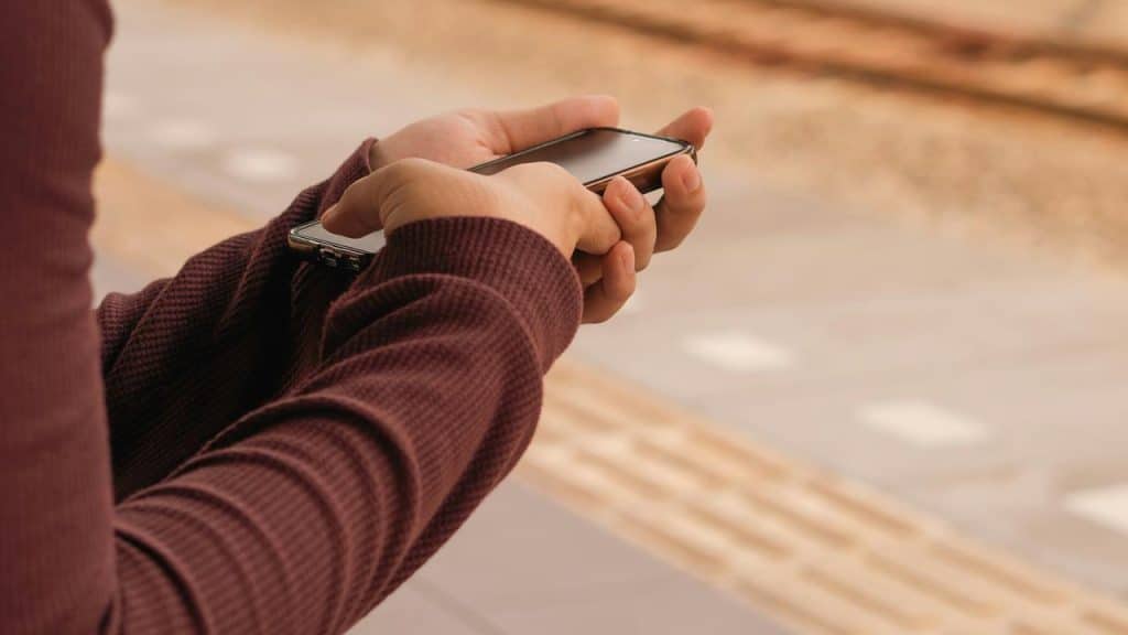 A person holding a smartphone while standing near train tracks.