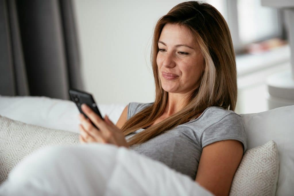 The woman is smiling while looking at her phone.
