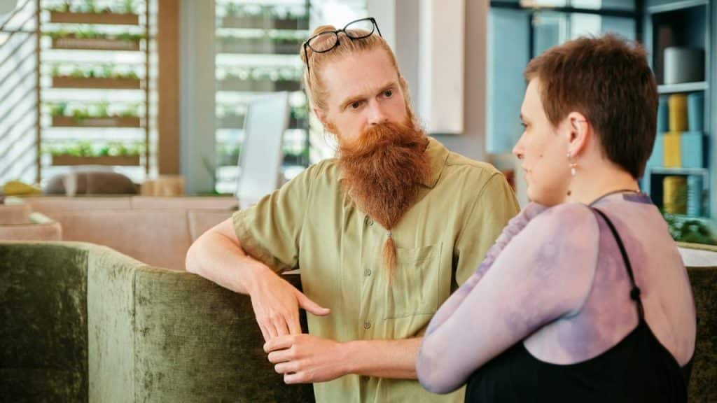 A man with a long red beard and glasses on his head talks to a woman.