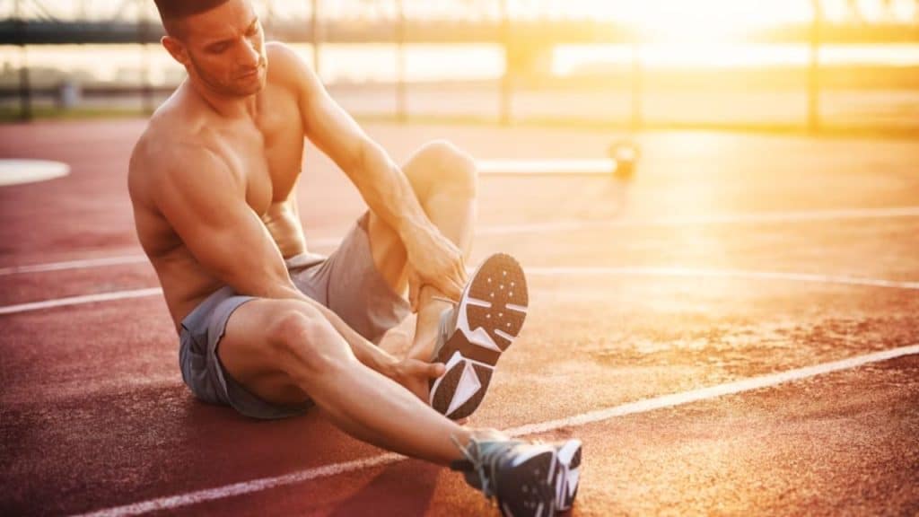 Man removing shoes after exercising outdoors, determined look, sunrise background