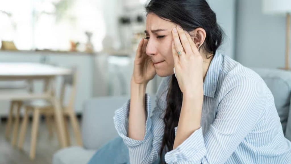 Woman rubbing her temples while sitting at the couch