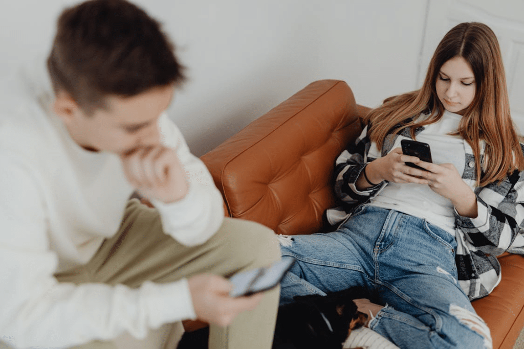 Boy and Girl Sitting on a Couch and Using Smartphones