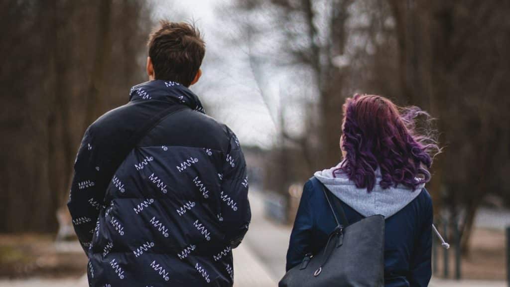 Man in a patterned black puffer jacket walks next to a woman with purple hair.
