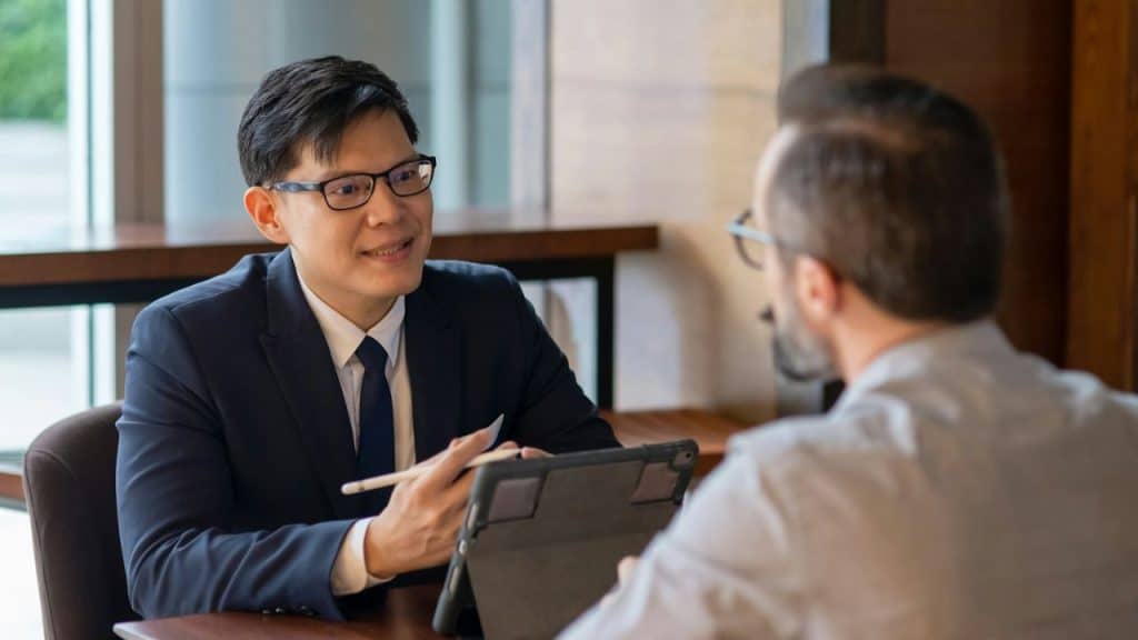 Asian man in a suit and glasses smiles, pointing a stylus at a tablet screen.