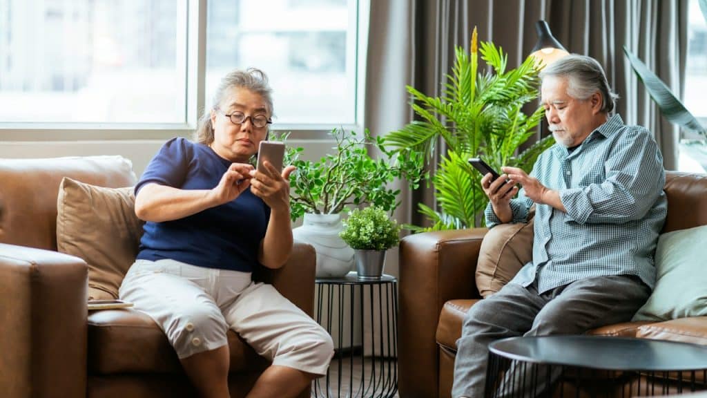 An Elderly couple using smartphones in their living room.