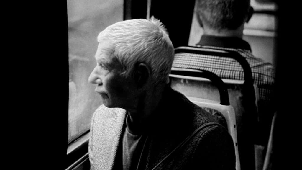 An old man looking outside while sitting in a bus.