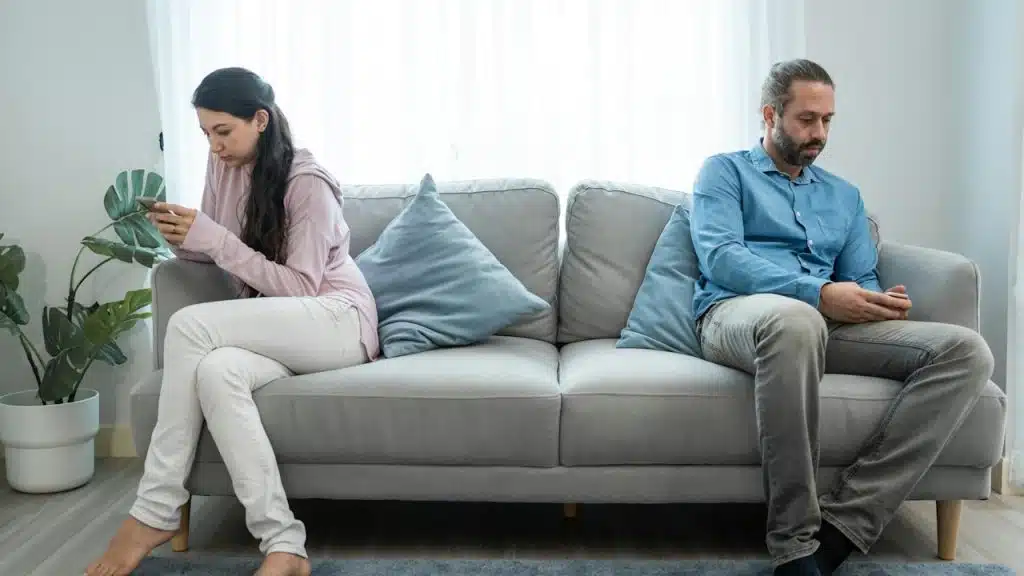 A couple sitting apart from each other on a couch and using their phones.