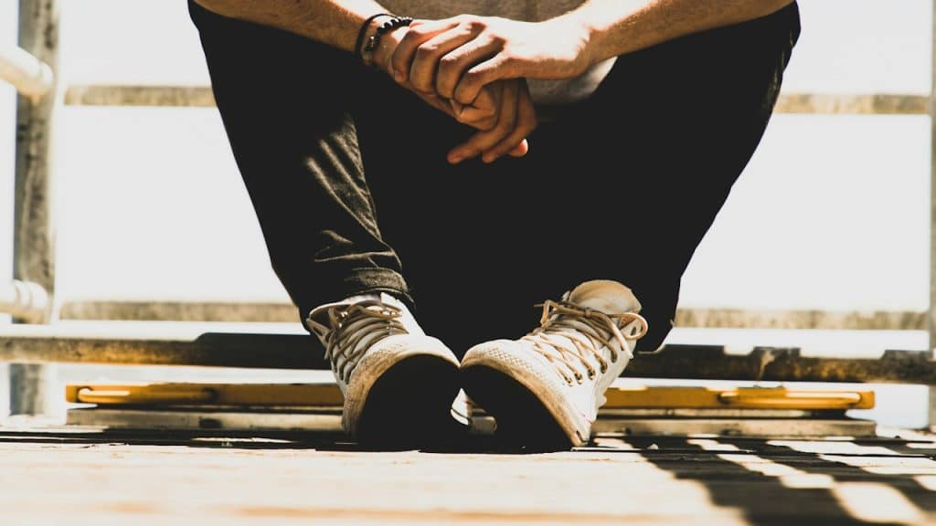 The lower body of a thoughtful man sitting on the floor.