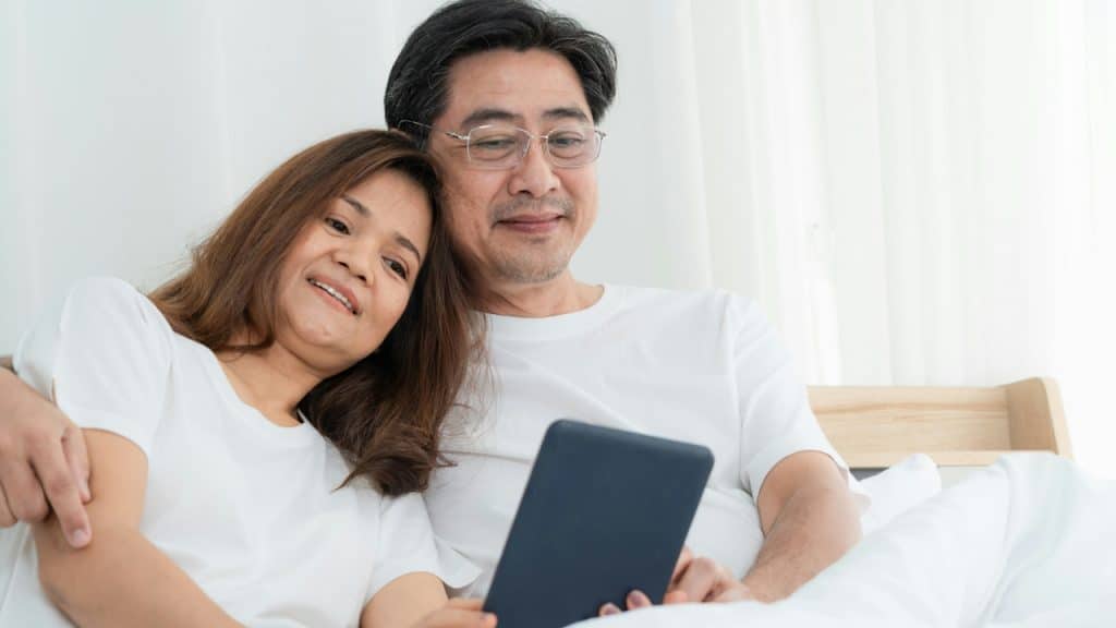 A happy couple looking at a tablet while in bed.