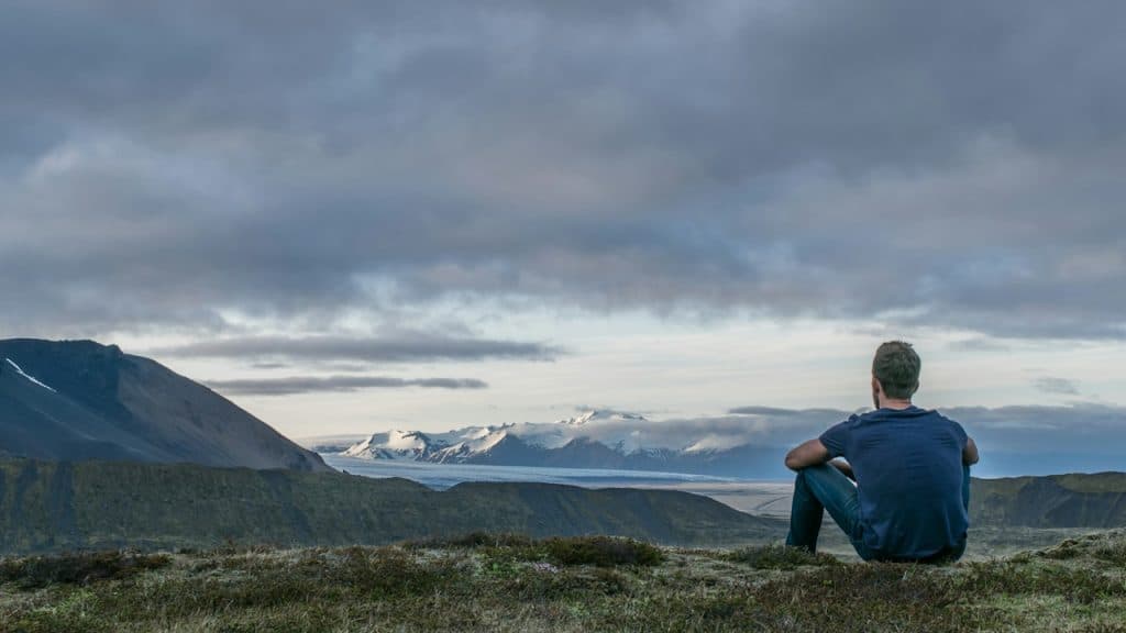 A man sitting on a cliff and gazing at a picturesque view of mountains.