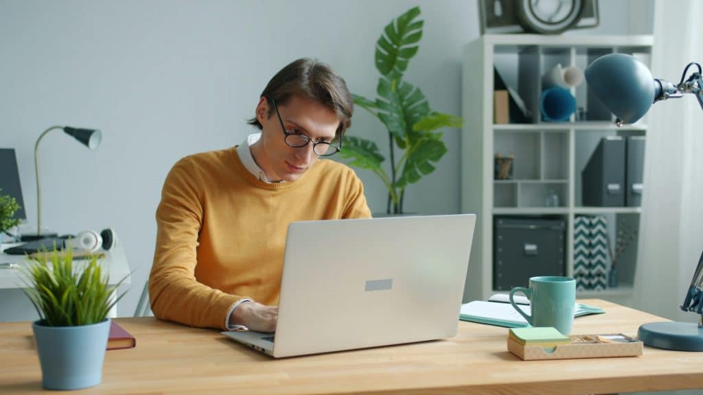 The man in the yellow sweater is working on a laptop.