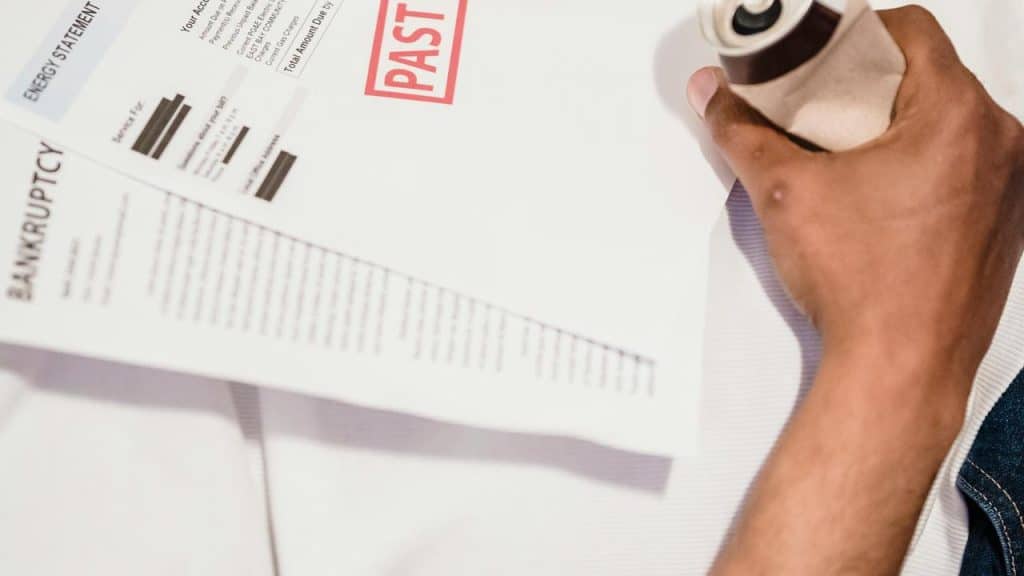 A person holding a coffee cup beside papers labeled bankruptcy and past due.