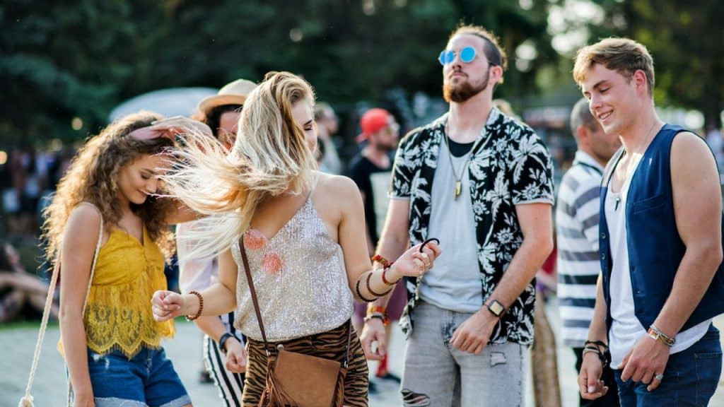 A group of young adults is dancing and smiling outdoors at a summer festival.