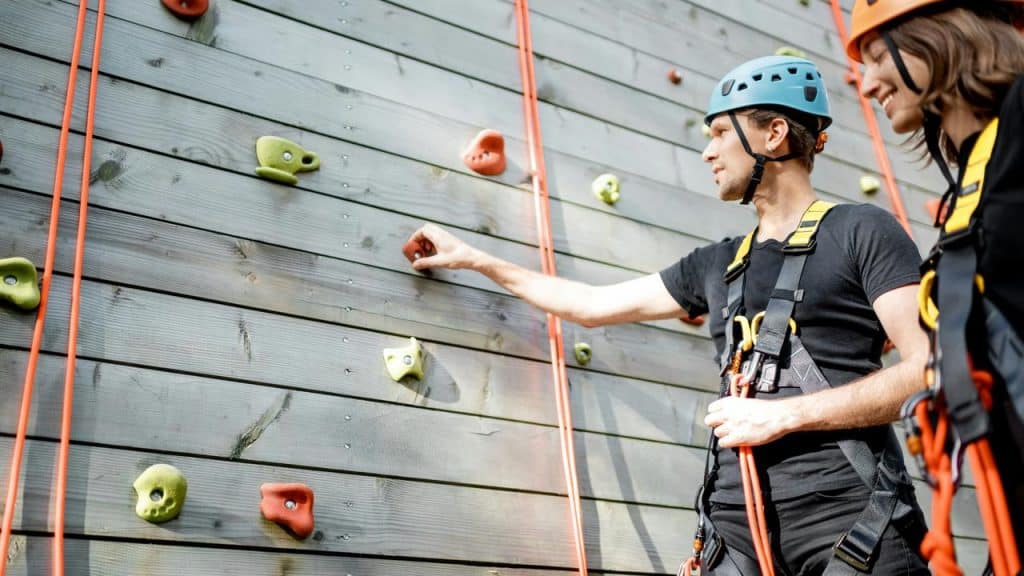 A couple wearing helmets and harnesses preparing to climb an outdoor rock wall.