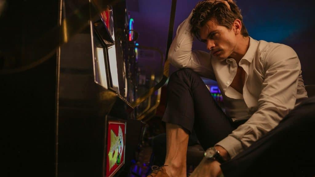 Man in white shirt, navy pants, and watch sits tensely by a brightly lit machine.